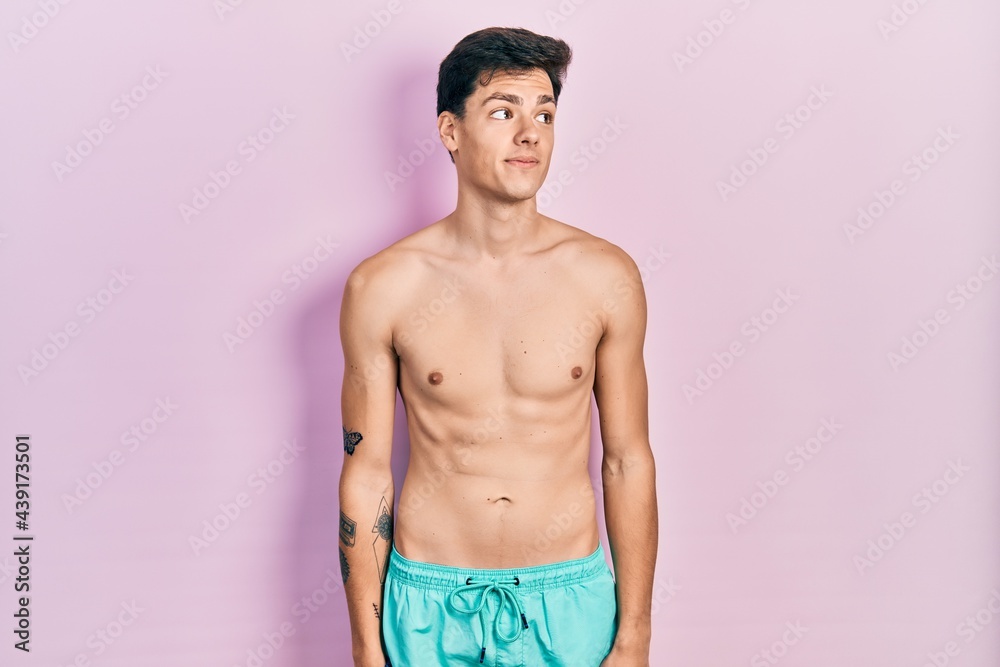 Fototapeta premium Young hispanic man wearing swimwear shirtless smiling looking to the side and staring away thinking.