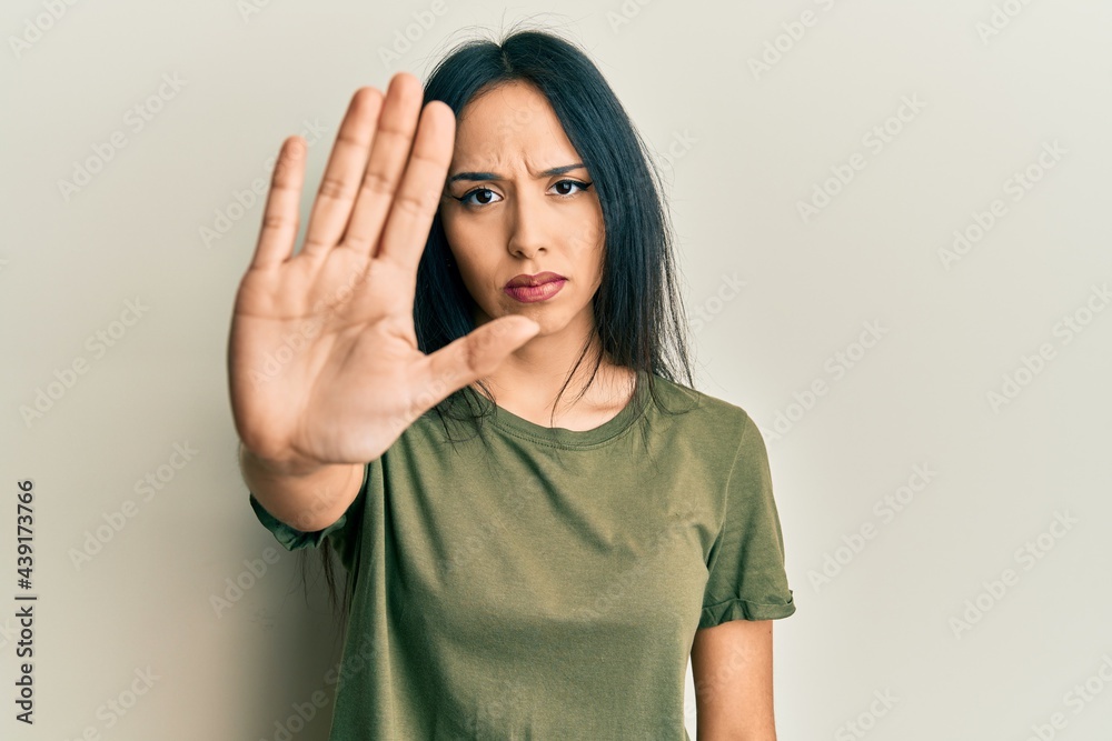 Young hispanic girl wearing casual t shirt doing stop sing with palm of the hand. warning expression with negative and serious gesture on the face. Young hispanic girl wearing casual t shirt doing stop sing with palm of the hand. warning expression with negative and serious gesture on the face.