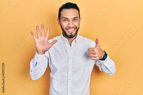 Hispanic man with beard wearing business shirt showing and pointing up with fingers number six while smiling confident and happy. © Krakenimages.com