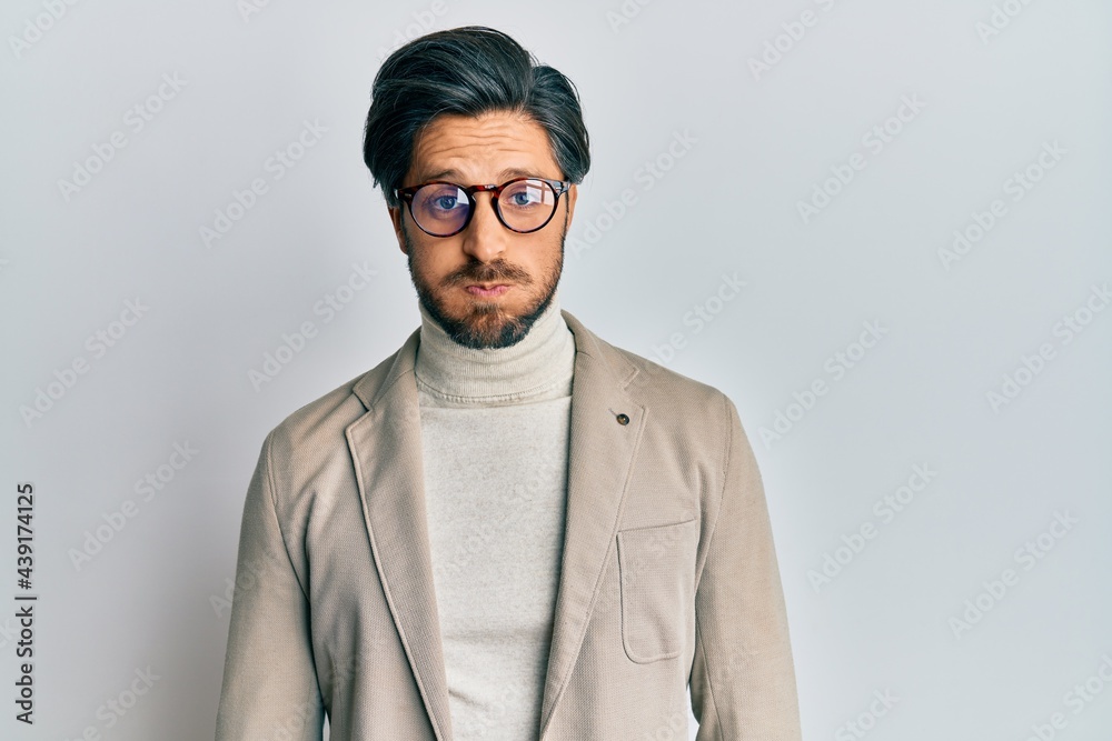 Young hispanic man wearing business jacket and glasses puffing cheeks with funny face. mouth inflated with air, crazy expression. Young hispanic man wearing business jacket and glasses puffing cheeks with funny face. mouth inflated with air, crazy expression.