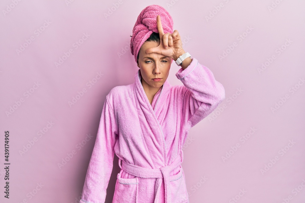 Young blonde woman wearing shower towel cap and bathrobe making fun of people with fingers on forehead doing loser gesture mocking and insulting. Young blonde woman wearing shower towel cap and bathrobe making fun of people with fingers on forehead doing loser gesture mocking and insulting.