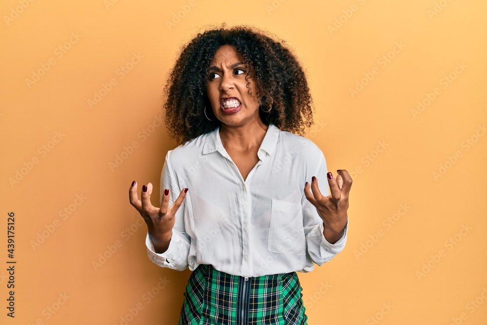 Beautiful african american woman with afro hair wearing scholar skirt crazy and mad shouting and yelling with aggressive expression and arms raised. frustration concept. Beautiful african american woman with afro hair wearing scholar skirt crazy and mad shouting and yelling with aggressive expression and arms raised. frustration concept.