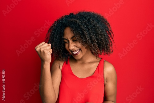 Beautiful african american woman with afro hair wearing casual clothes celebrating surprised and amazed for success with arms raised and eyes closed