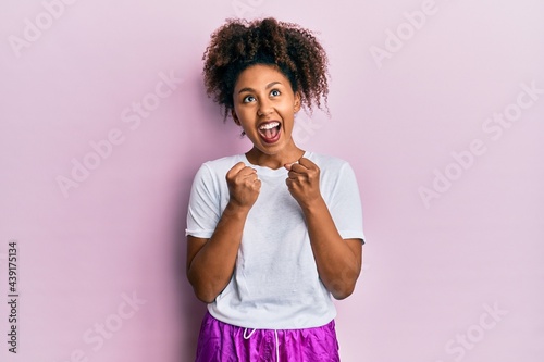 Beautiful african american woman with afro hair wearing sportswear celebrating surprised and amazed for success with arms raised and open eyes. winner concept.