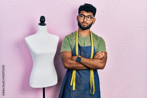 Arab man with beard dressmaker designer wearing atelier apron smiling looking to the side and staring away thinking.