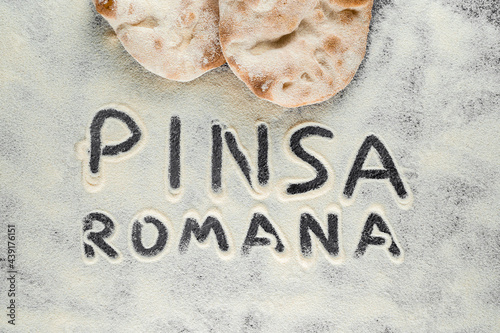 Dough and flour with text pinsa romana on black background. Scrocchiarella gourmet italian cuisine. Traditional dish in italy. photo