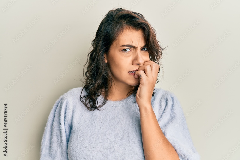Young hispanic woman wearing casual winter sweater looking stressed and nervous with hands on mouth biting nails. anxiety problem. Young hispanic woman wearing casual winter sweater looking stressed and nervous with hands on mouth biting nails. anxiety problem.