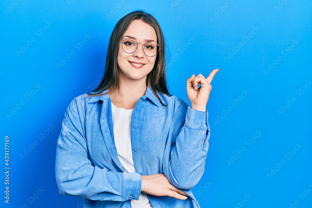 Young hispanic girl wearing casual clothes and glasses smiling happy pointing with hand and finger to the side Young hispanic girl wearing casual clothes and glasses smiling happy pointing with hand and finger to the side