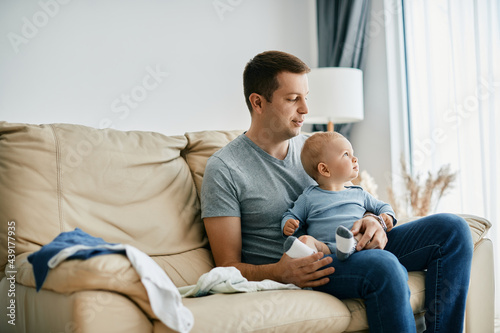 Young father and his baby son relaxing in living room. Smiling father sitting on the sofa with his baby boy while spending time with him at home. © Drazen