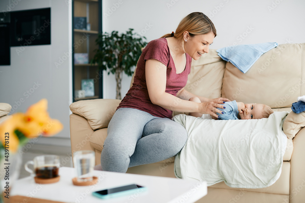 Young happy mother talking to her baby son who is lying on the sofa and looking at camera. Young happy mother talking to her baby son who is lying on the sofa and looking at camera.