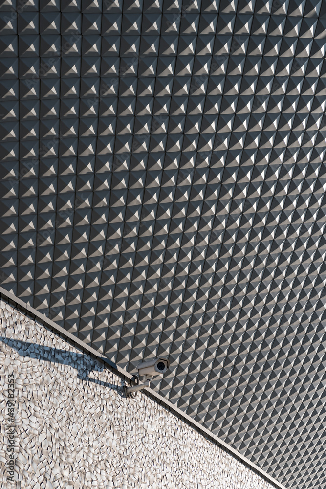 Street camera attached to a building, geometric elevation tiles in background