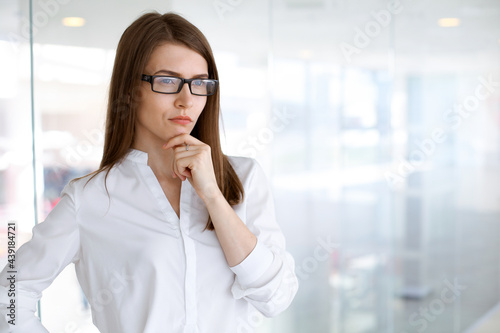 Beautiful female specialist with dark hair standing in modern office and smiling charmingly. Working on design, data analysis, plan strategy. Business people concept