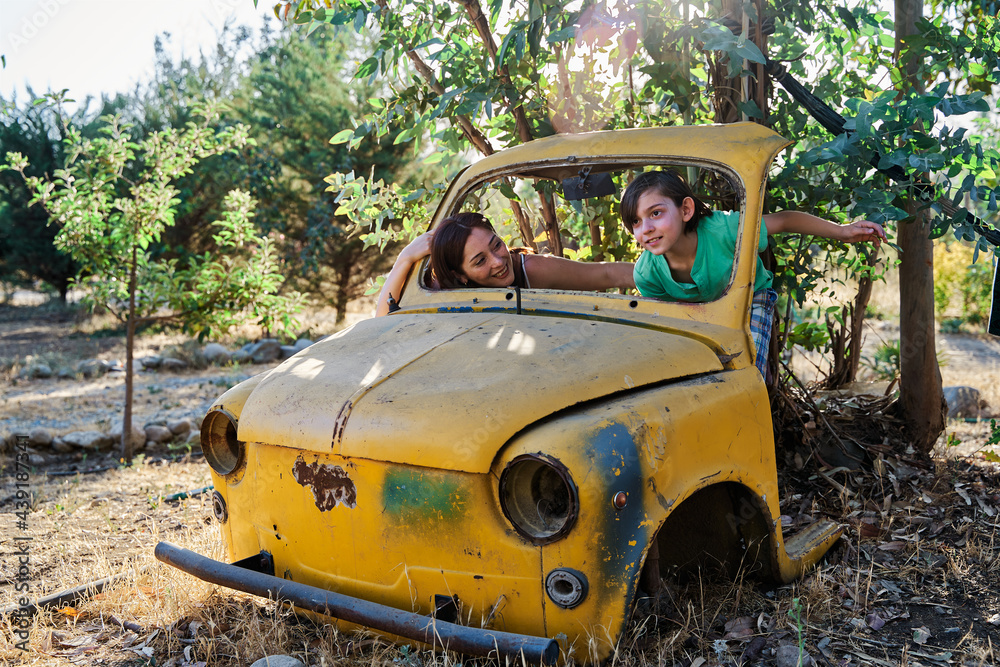 portrait of a mother and child playing inside the wreckage of a yellow junk truck on a sunny day, concept of family life. portrait of a little boy playing at pruning a tree with his mother on a sunny portrait of a mother and child playing inside the wreckage of a yellow junk truck on a sunny day, concept of family life. portrait of a little boy playing at pruning a tree with his mother on a sunny
