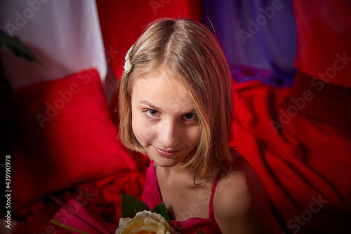 Young teen blonde girl with flowers in red room. Spring portrait. Healthy skin and natural makeup for teenage girls
