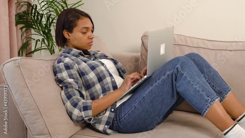 A tired young African-American woman is typing text at home on a laptop. The concept of fatigue and stress, freelance.