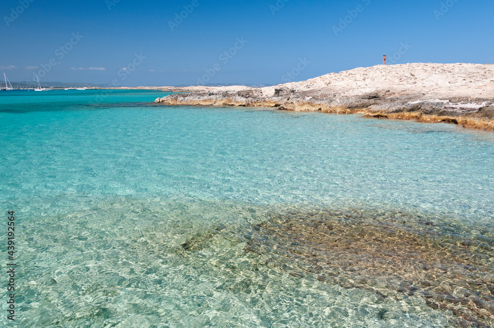 The beach of Ses Illetas, Formentera, Spain. A person in the top of the rock observes the crystal clear the Mediterranean Sea