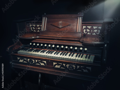 Beautiful old wooden piano and black finishes along with a spotlight that illuminates its design. Retro piano, classic style. Instrumental classical music. Classic culture. Vintage, retro, obsolete. photo