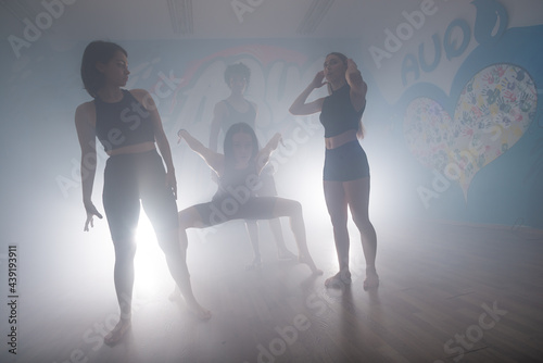 Group of multiracial dancers enjoying funky hip hop moves in dark studio with smoke and lighting. Group of young hip-hop dancers performing on the stage. Happy dancing women.