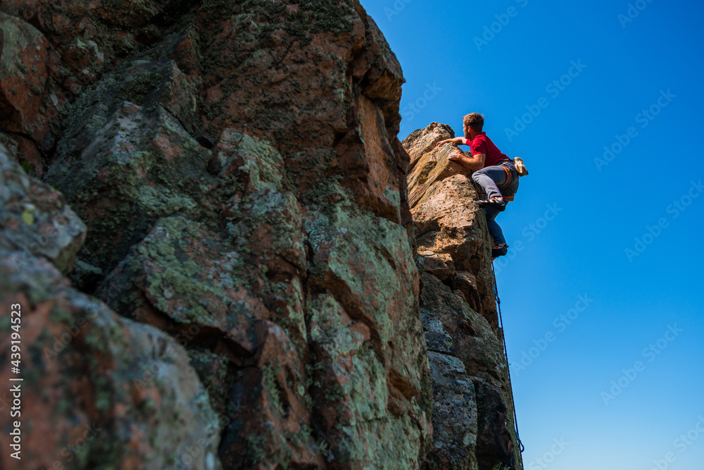 Young rock climber climbs the cliff with a belay