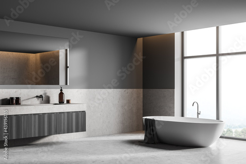 Bathroom interior with bathtub near window and sink with mirror  grey floor