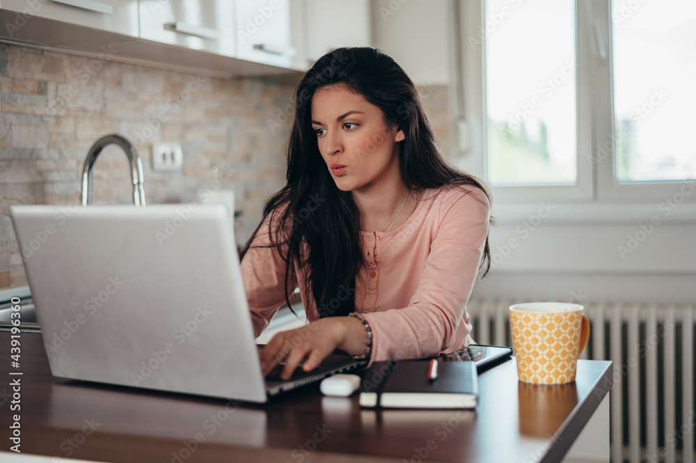 Young gorgeous woman using a laptop and drinking coffee in the morning in the kitchen Young gorgeous woman using a laptop and drinking coffee in the morning in the kitchen