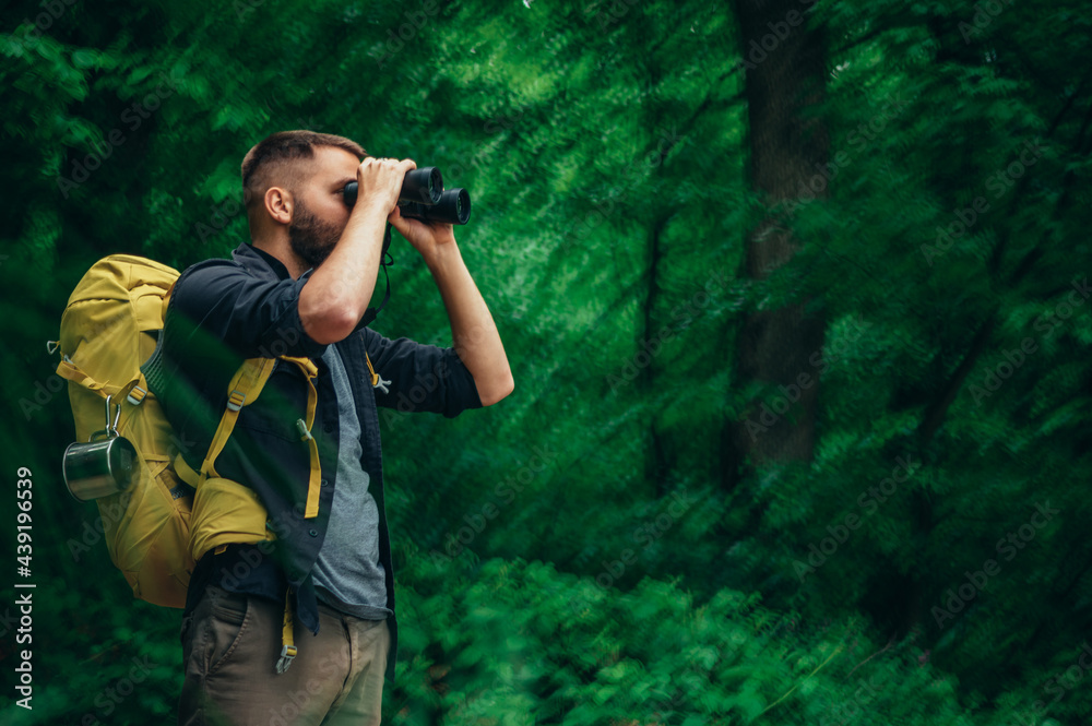 Young hiker using binoculars while walking in the forest