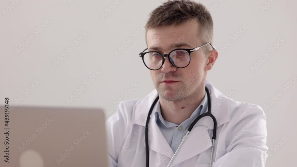 telemedicine, a European doctor in a white coat and glasses reads information about a patient's illness on a laptop, a notebook record of the patient's medical history, a Caucasian doctor in a telemedicine, a European doctor in a white coat and glasses reads information about a patient's illness on a laptop, a notebook record of the patient's medical history, a Caucasian doctor in a