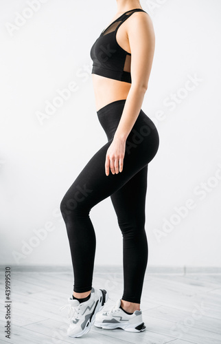 Female sportswear. Active lifestyle. Workout apparel. Side view of unrecognizable slim athletic woman body in black crop top bra leggings on light background.