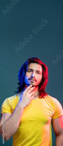Hipster man. Neon light portrait. Metrosexual fashion. Trend model look. Stylish dreamful bearded guy yellow t-shirt holding chin in blue red vibrant color isolated deep ocean.