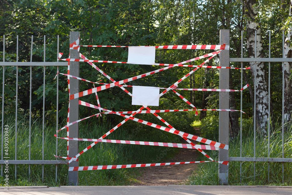 Barrier tape at the entrance to the city park, blank white sheets of paper for messages. Barrier tape at the entrance to the city park, blank white sheets of paper for messages.