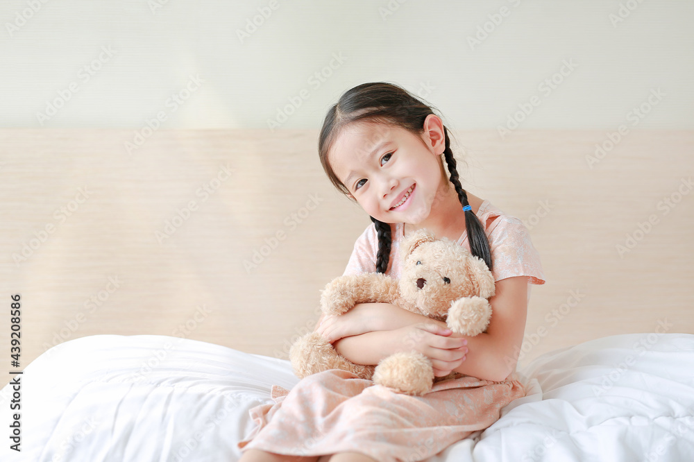 Smiling Asian little girl cuddle teddy bear and looking camera while sitting on the bed at home. Smiling Asian little girl cuddle teddy bear and looking camera while sitting on the bed at home.