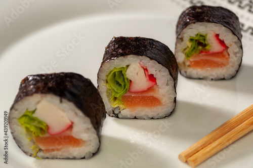Three sushi rolls on a white plate with chopsticks
