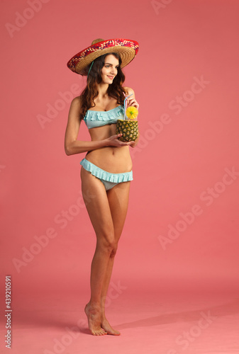 young beautiful woman in bikini and sombrero with exotic tropic cocktail isolated on pink background