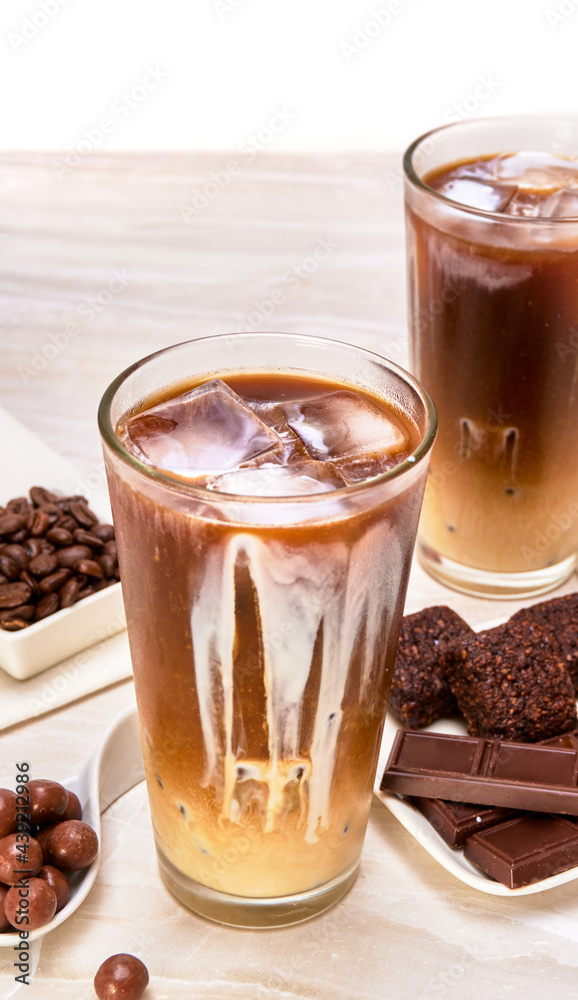 iced latte macchiato accompanied by chocolate pearls, vegan brownies and chocolate bars on a marble surface and white background. luxury concept. copy space for advertising. close up view iced latte macchiato accompanied by chocolate pearls, vegan brownies and chocolate bars on a marble surface and white background. luxury concept. copy space for advertising. close up view
