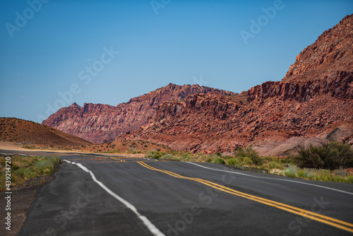 Desert highway at sunset, travel concept, USA. Landscape with orange rocks, sky with clouds and asphalt road in summer. American roadtrip.