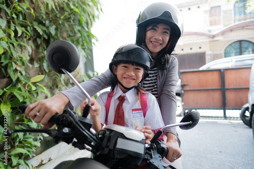 mother taking her daughter to school by motorcycle in the morning. asian primary student wearing uniform going back to school