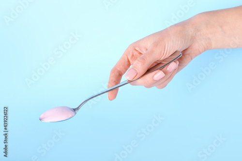 Female hand with spoon of tasty yogurt on color background