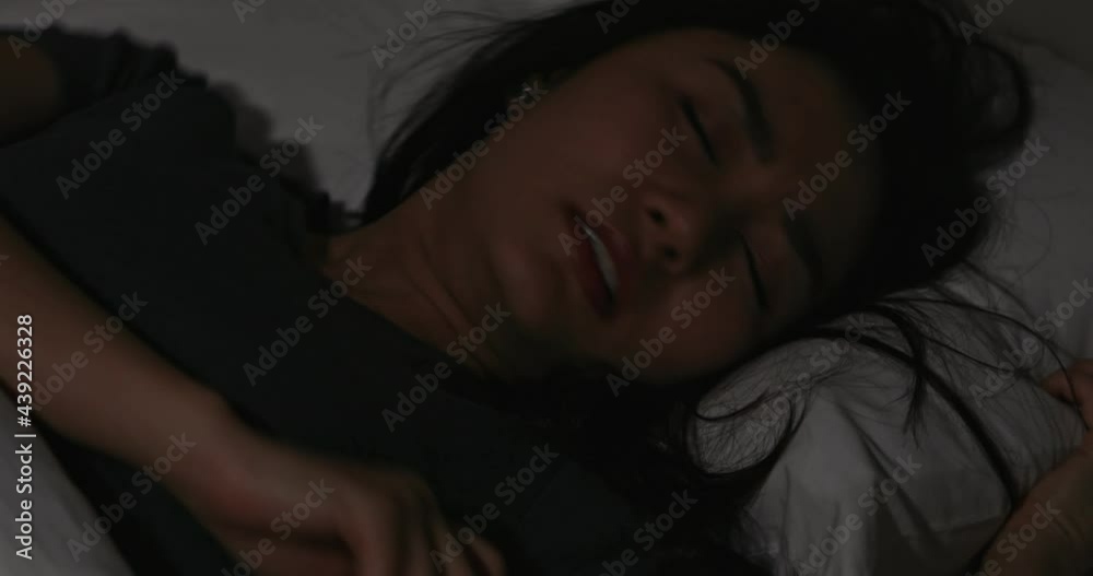 Young Asian woman sleeping on bed in bedroom at night and falling in bad dream nightmare and turn around her body with stress and frustrated.
