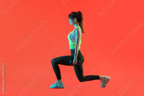 Sporty young woman training with dumbbells on color background