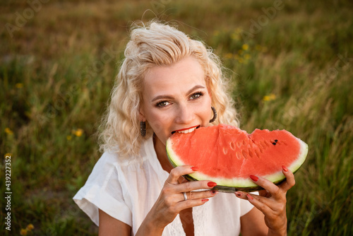 Close-up portrait of a woman biting a watermelon in nature. Beautiful girl of caucasian appearance eats a watermelon on a picnic.