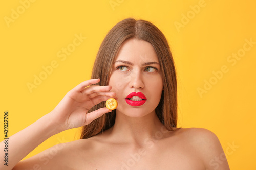 Beautiful young woman with sweet cumquat on color background