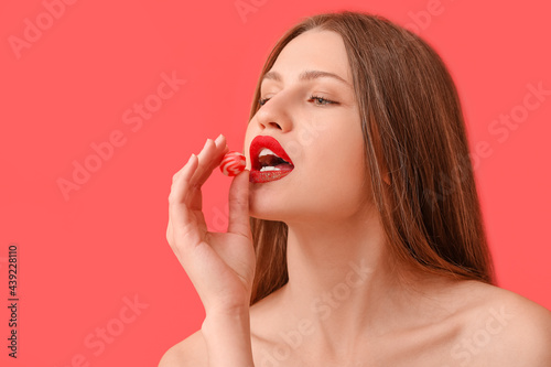 Beautiful young woman with sweet candy on color background