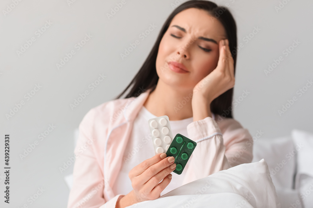 Young woman with pills suffering from headache in bedroom Young woman with pills suffering from headache in bedroom