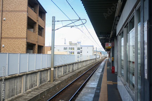 Empty platform and rail track at a small train station in Japan. Clouds in blue sky. No people. Perspective view.