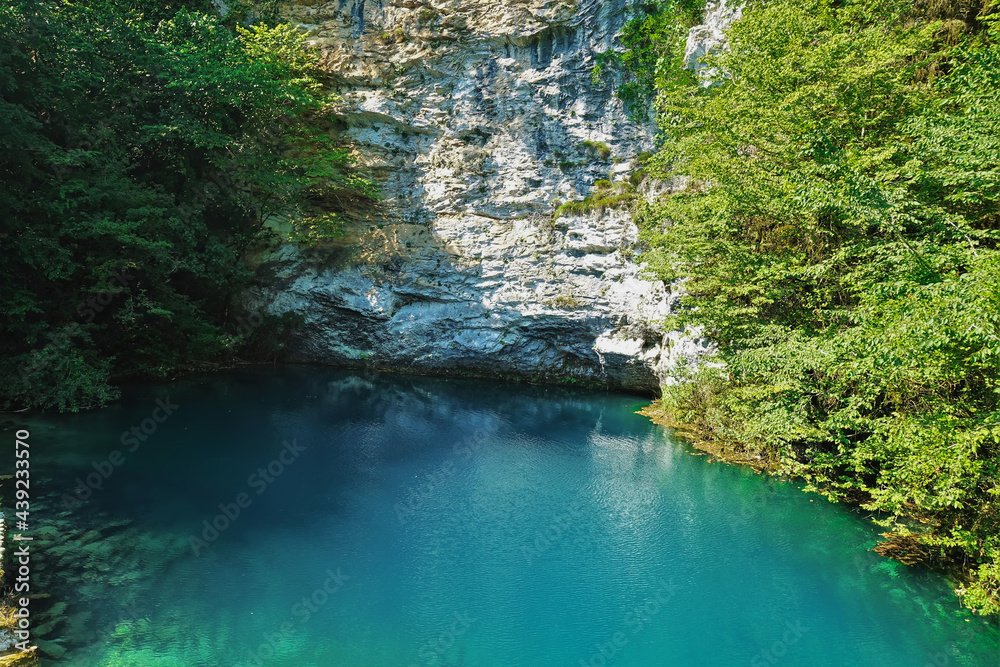 The alpine lake is surrounded by sheer cliffs with green vegetation. Reflection and shadows on calm aquamarine water. Blue Lake. Abkhazia