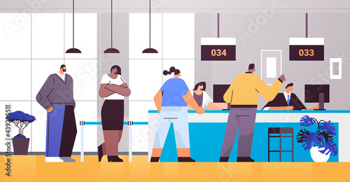 mix race people looking at display number board in waiting room with ticket system electronic queuing system