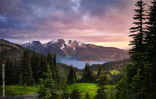 Glacial mountain Garibaldi lake at sunset. View of a mountain lake between fir trees. Mountain peaks above the lake lit by sunset rays. Garibaldi Provincial Park. Canada
