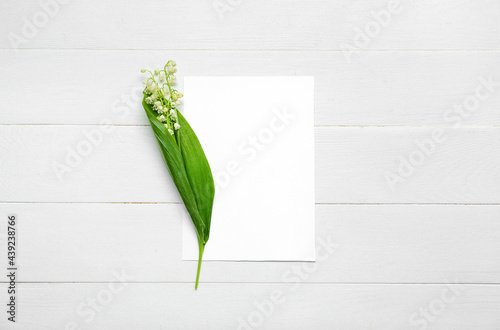 Beautiful lily-of-the-valley flowers and blank card on light wooden background