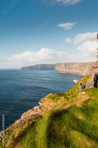 Amazing view on Cliff of Moher, county Clare, Ireland. Popular landmark with unparalleled scenery. Warm sunny day, Cloudy sky. Calm water of Atlantic ocean. Verticla image photo