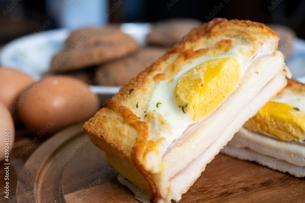 Croque madame or monsieur. Toast, with fried eggs, ham, cheese, and hollandaise sauce. Sandwich with Egg, ham and cheese on wooden plate on a table. Half croque monsieur on plate. Croque madame or monsieur. Toast, with fried eggs, ham, cheese, and hollandaise sauce. Sandwich with Egg, ham and cheese on wooden plate on a table. Half croque monsieur on plate.